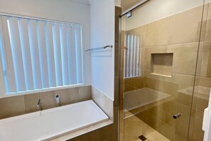 Un bagno moderno con vasca, box doccia in vetro e finestra con persiane.