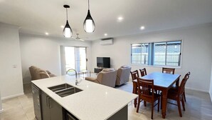 Cocina moderna con una isla central, comedor con sillas de madera, televisor de pantalla plana y un ventanal grande.