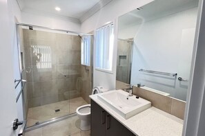 A modern bathroom with a glass shower enclosure, a white sink, and a large mirror. - New  4Bed House master with ensuite and A/C (Collingwood Park)
