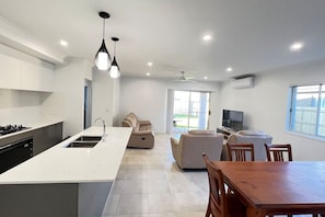 Una cocina moderna con una isla central, una zona de comedor con mesa de madera y una sala de estar con sofá.