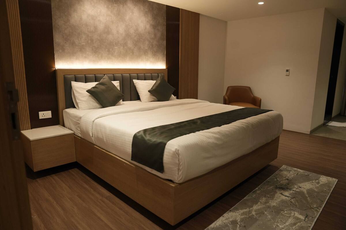 A modern bedroom with a large bed, a nightstand, a chair, and a textured rug.