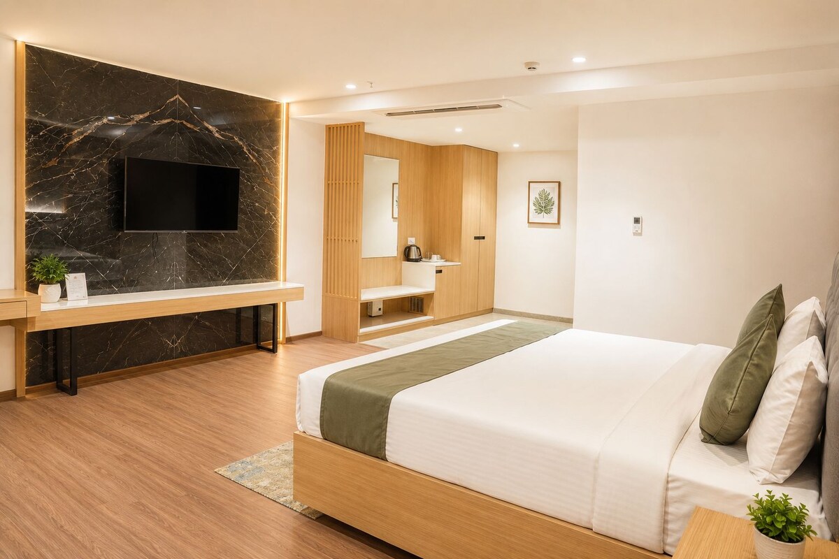 Een moderne hotelkamer met een groot bed, een houten bureau, een flatscreen televisie, een houten garderobe en een badkamer met een spiegel en wastafel.