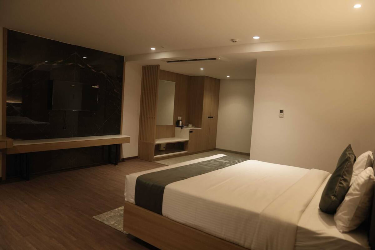 A modern bedroom with a large bed, wooden flooring, a vanity with a mirror, and recessed ceiling lighting.