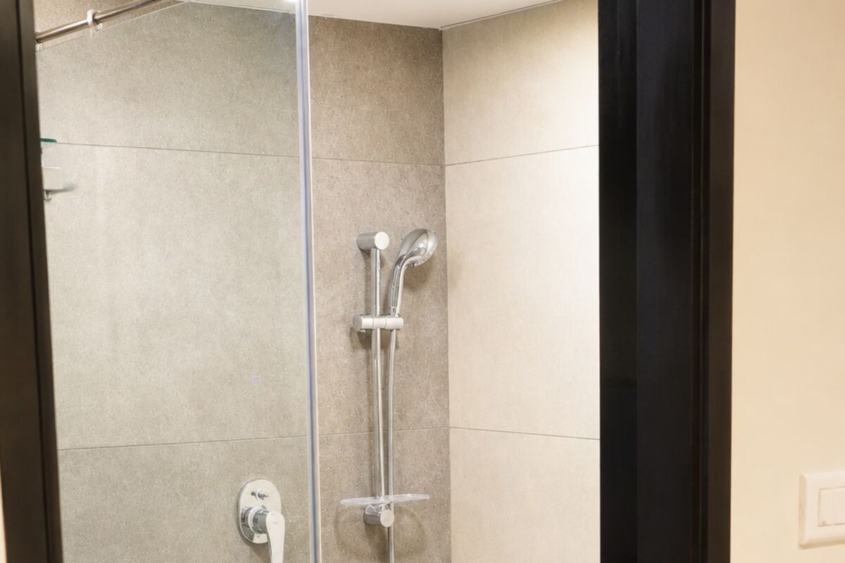 Een douchecabine met glazen wanden, een handdouche en een wandmengkraan.