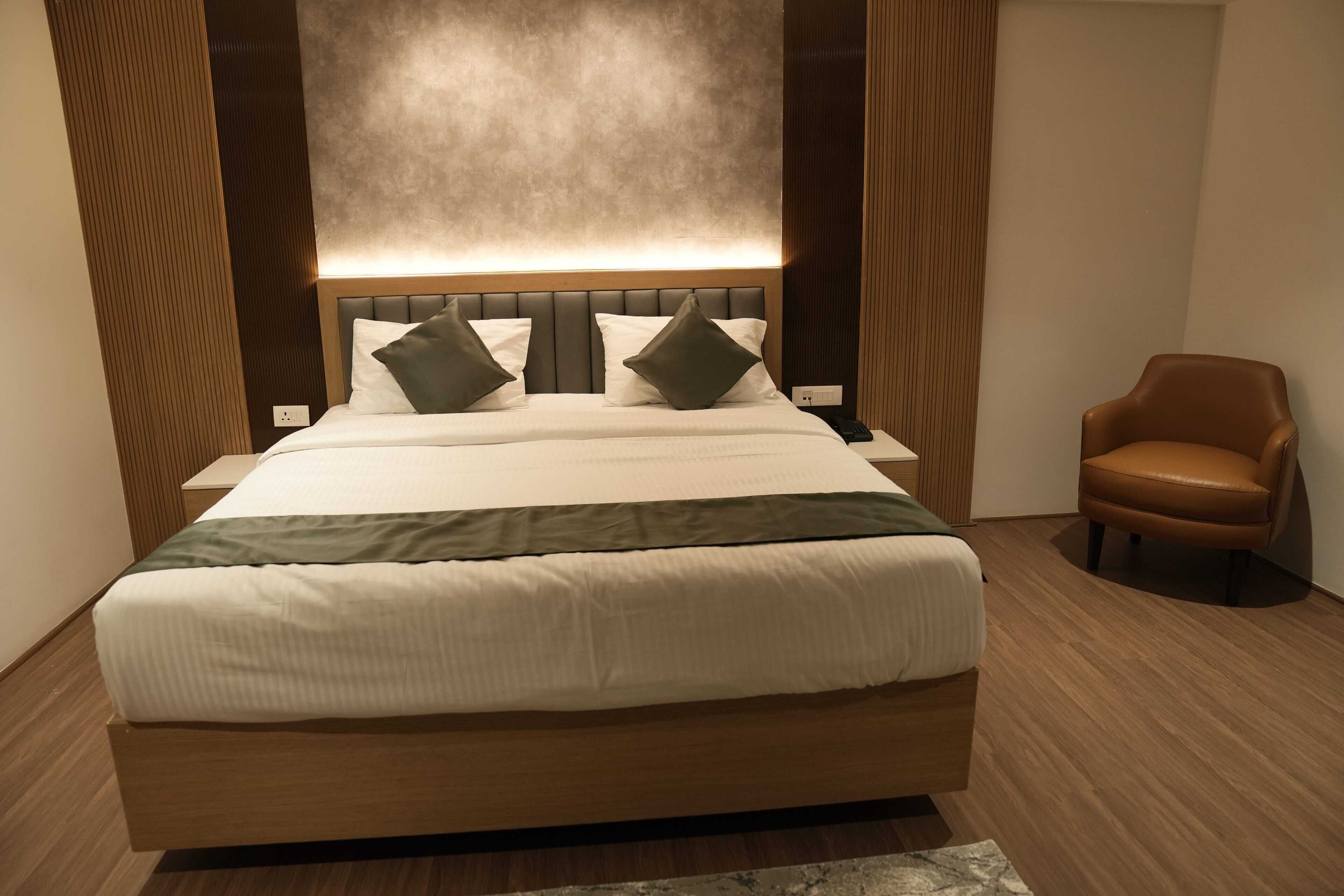 Una habitación de hotel moderna con una cama grande, un cabecero de madera y un sillón de cuero marrón.