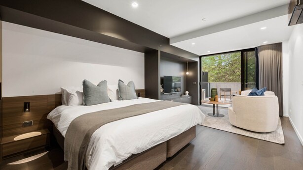 A modern bedroom with a large bed, a seating area, and a view of the outdoors. - Stylish Studio in Braddon With Communal Area (Canberra)