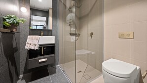 A modern bathroom with a glass-enclosed shower, a white toilet, and a vanity with a sink and mirror. - Stylish Studio in Braddon With Communal Area (Canberra)