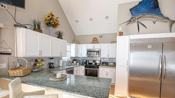 Una cocina moderna con armarios blancos, encimera de granito, electrodomésticos de acero inoxidable y un mural decorativo de peces.