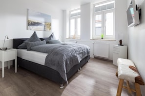 A bedroom with a bed, bedside tables, a TV, and a window.