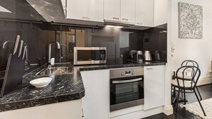 A compact kitchen with white cabinets, a black countertop, stainless steel appliances, and a small dining area with a chair. - Cosy and Central City Studio Near Attractions (Melbourne)