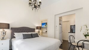 A bedroom with a large bed, a chandelier, a television, and a dining area with chairs. - Cosy and Central City Studio Near Attractions (Melbourne)
