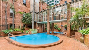 A swimming pool surrounded by brick walls and potted plants, with a glass bridge connecting two levels. - Cosy and Central City Studio Near Attractions (Melbourne)