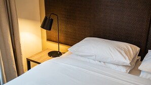 Un lit bien fait, avec du linge de lit blanc, une lampe de sol noire et une tête de lit à motifs.