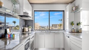 A modern kitchen with white cabinets, a large window, and a view of the city. - 2-bed Near Beach With BBQ & Stunning Ocean Views (Sunshine Coast)