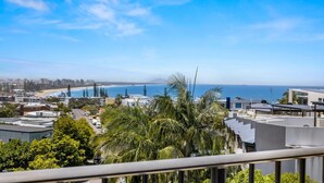 A coastal cityscape with modern buildings, a beach, and a clear blue sky. - 2-bed Near Beach With BBQ & Stunning Ocean Views (Sunshine Coast)