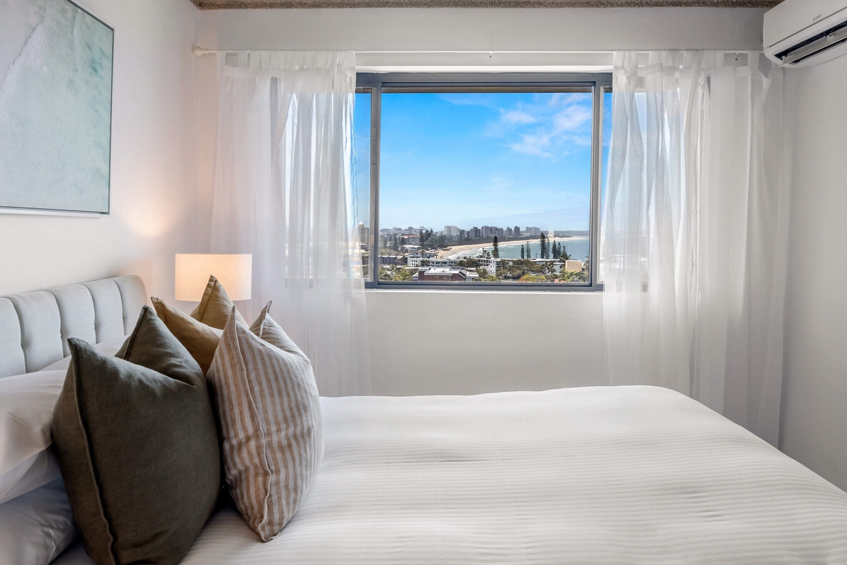 A bedroom with a large bed, a view of a cityscape through a window, and a couch with pillows.