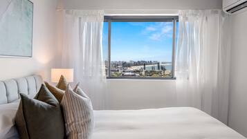 A bedroom with a large bed, a view of a cityscape through a window, and a couch with pillows.