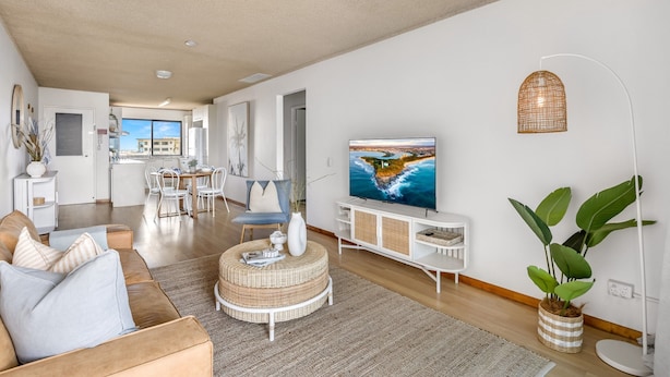 A modern living room with a sofa, a round coffee table, a television, and a large plant. - 2-bed Near Beach With BBQ & Stunning Ocean Views (Sunshine Coast)