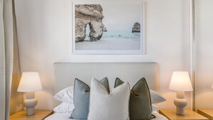 A neatly made bed with pillows and a framed picture of a coastal landscape above it. - 2-bed Near Beach With BBQ & Stunning Ocean Views (Sunshine Coast)