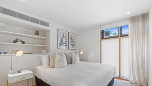 Un dormitorio moderno con una cama grande, mesitas de noche, un estante empotrado con objetos decorativos y una ventana con cortinas.