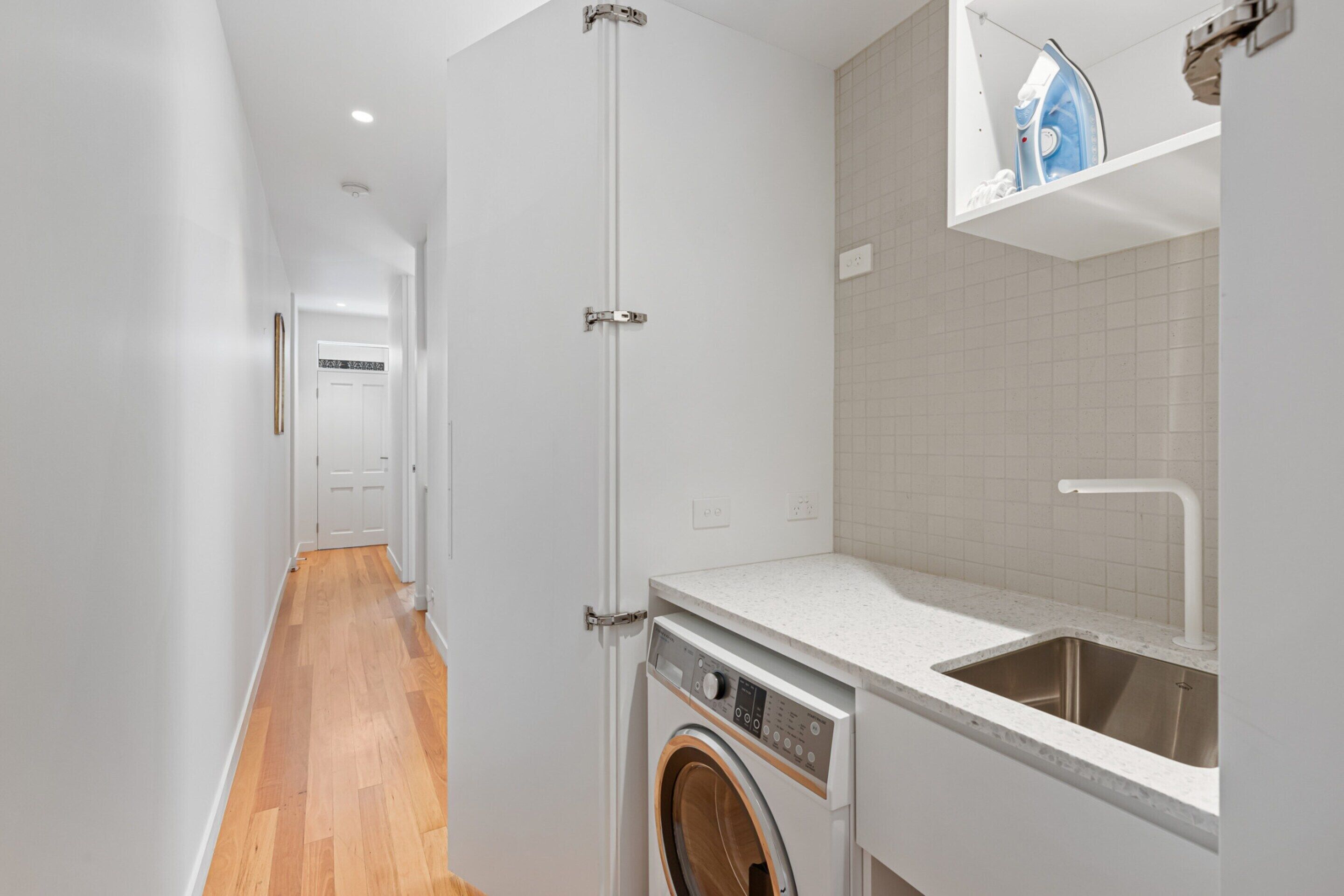 A laundry area with a washing machine, a sink, and a door leading to another room.