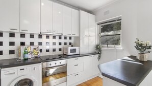 Una cocina moderna con armarios blancos, microondas integrado, lavadora y ventana con vistas a zonas verdes.