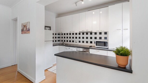 Una cocina moderna con armarios blancos, encimera negra y un microondas.