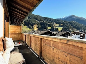 En træterrasse med en sofa og et bord, med udsigt over et bjerglandskab med huse.