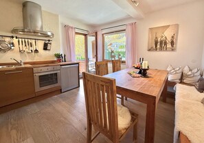 A kitchen with wooden cabinets, a stainless steel range hood, and a dining area with a wooden table and chairs. - Kitzhorn Emotions *near ski lift* by Belle-Stay (Jochberg)
