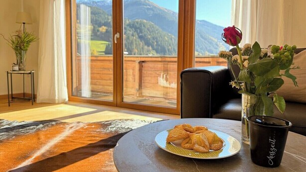 Quarto com vista para montanhas, uma mesa com doces, um vaso com flores e uma xícara de café.