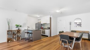 A modern kitchen with white cabinets, a central island, and a dining area with a wooden table and chairs. - Luxe 2-bed Apartment With River Views Near Casino (Melbourne)