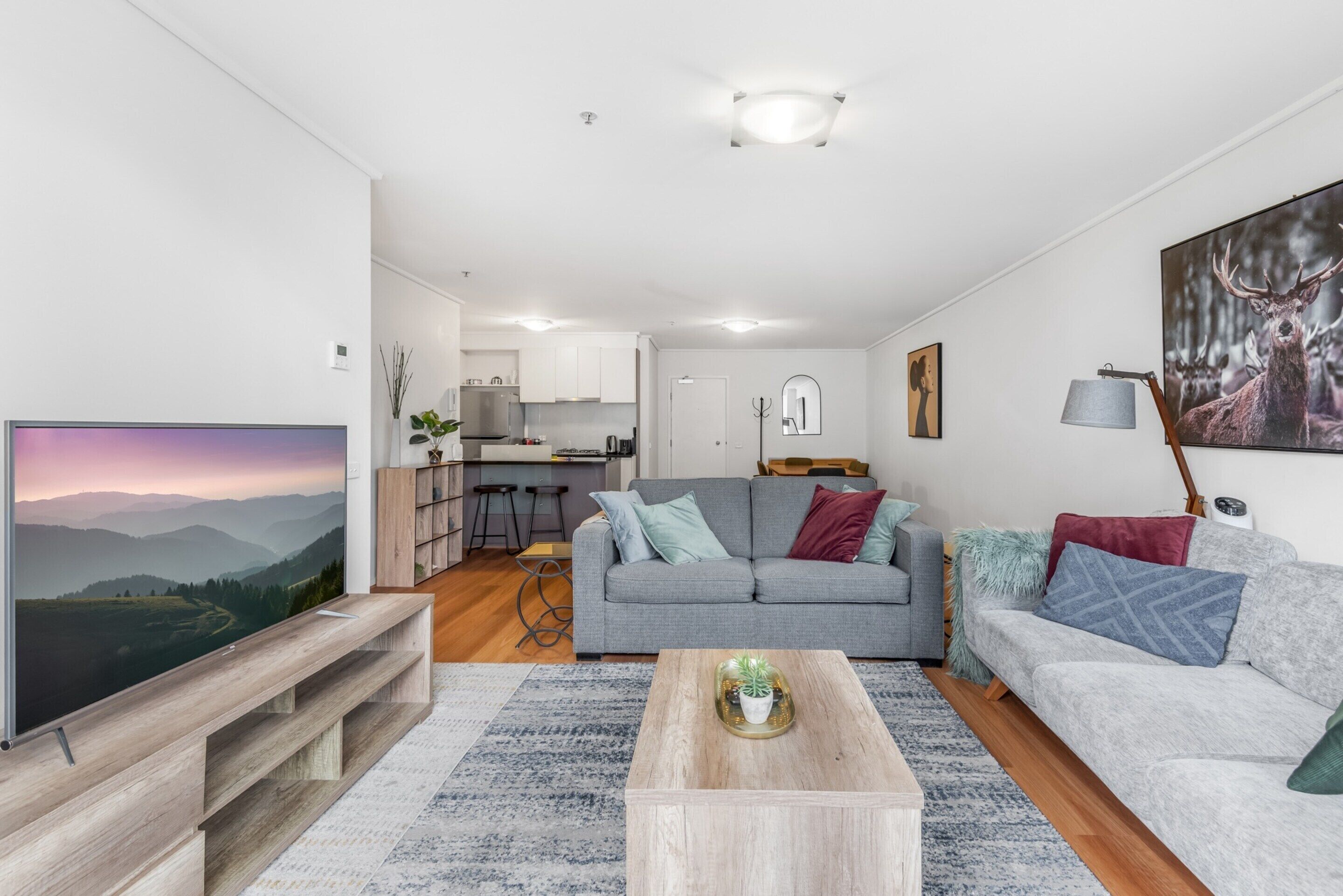 Ein modernes Wohnzimmer mit einem grauen Sofa, einem Couchtisch und einem Fernseher auf einem Holzgestell.