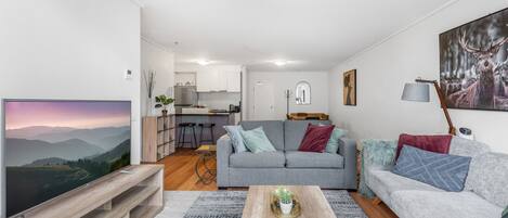 Ein modernes Wohnzimmer mit einem grauen Sofa, einem Couchtisch und einem Fernseher auf einem Holzgestell.