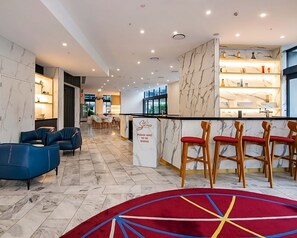 A modern hotel lobby with marble flooring, blue and red bar stools, and a reception desk. - Ocean View 2-bed With Pool, Sauna, (Gold Coast)