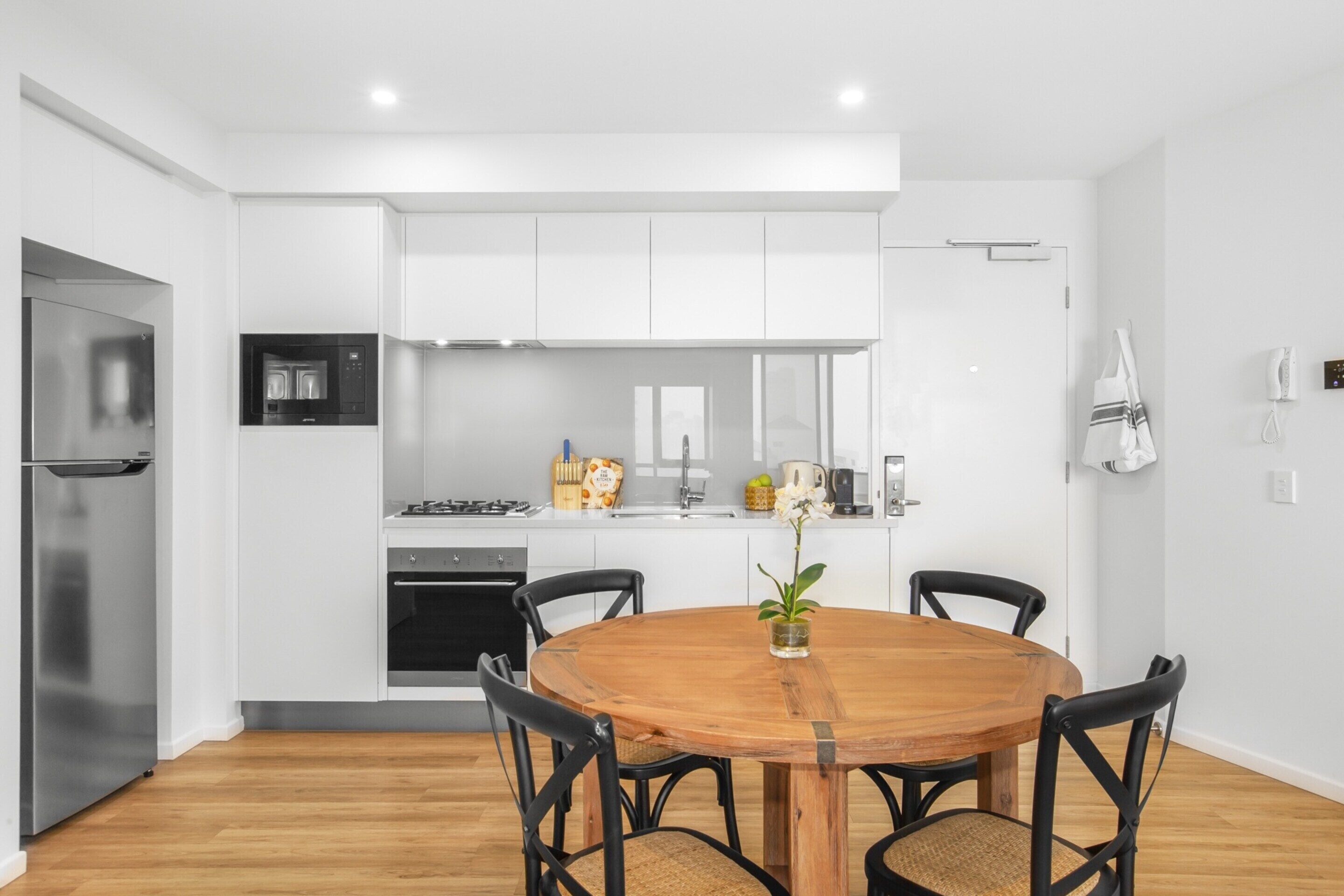 A modern kitchen with white cabinetry, a wooden dining table, and black chairs.