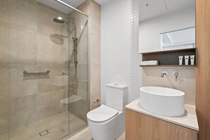 Een moderne badkamer met een douchecabine van glas, een wit toilet en een grote wastafel met een marmeren aanrecht.