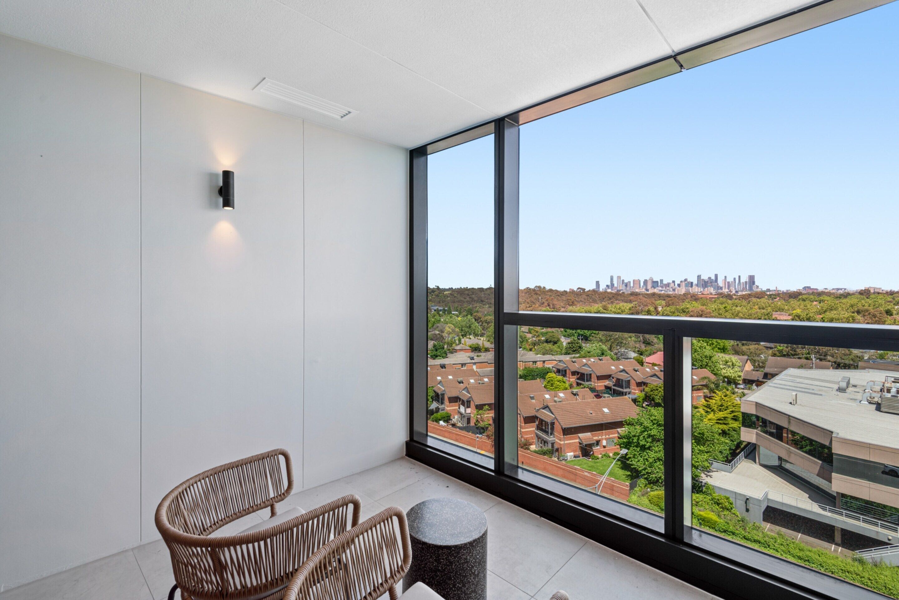 Ein Balkon mit Blick auf eine Stadtlandschaft, Weidekorbstühle und ein kleiner runder Tisch.