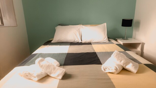 Un lit bien fait, avec une couverture à carreaux, deux oreillers et deux serviettes posées sur le lit.