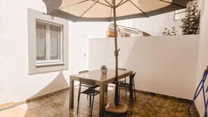 Une terrasse avec une table et des chaises, une plante en pot et une fenêtre.