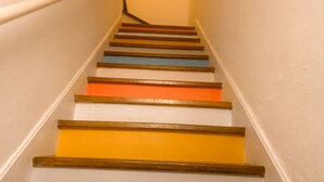 Un escalier dont les marches alternent des couleurs différentes, avec une main courante sur le côté gauche.
