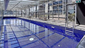 Une piscine intérieure dotée d’un toit en verre, de carreaux bleu clair et d’un banc.