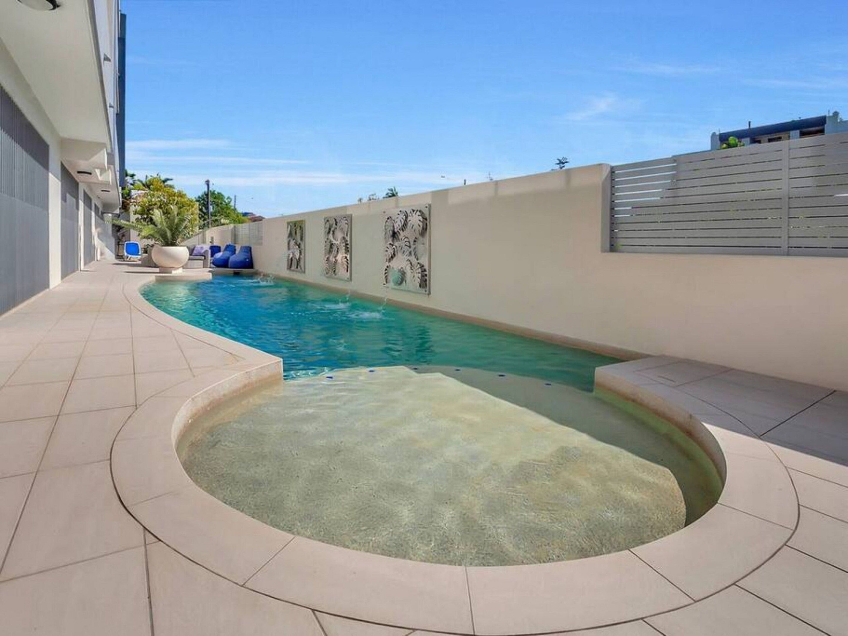 Una piscina con un jacuzzi, rodeada por un patio empedrado y una pared con paneles decorativos.