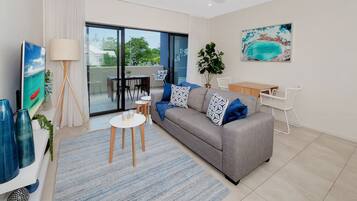 Un salon moderne avec un canapé gris, des coussins à motifs bleus et blancs, une table basse, un lampadaire et un tableau représentant un bateau accroché au mur.