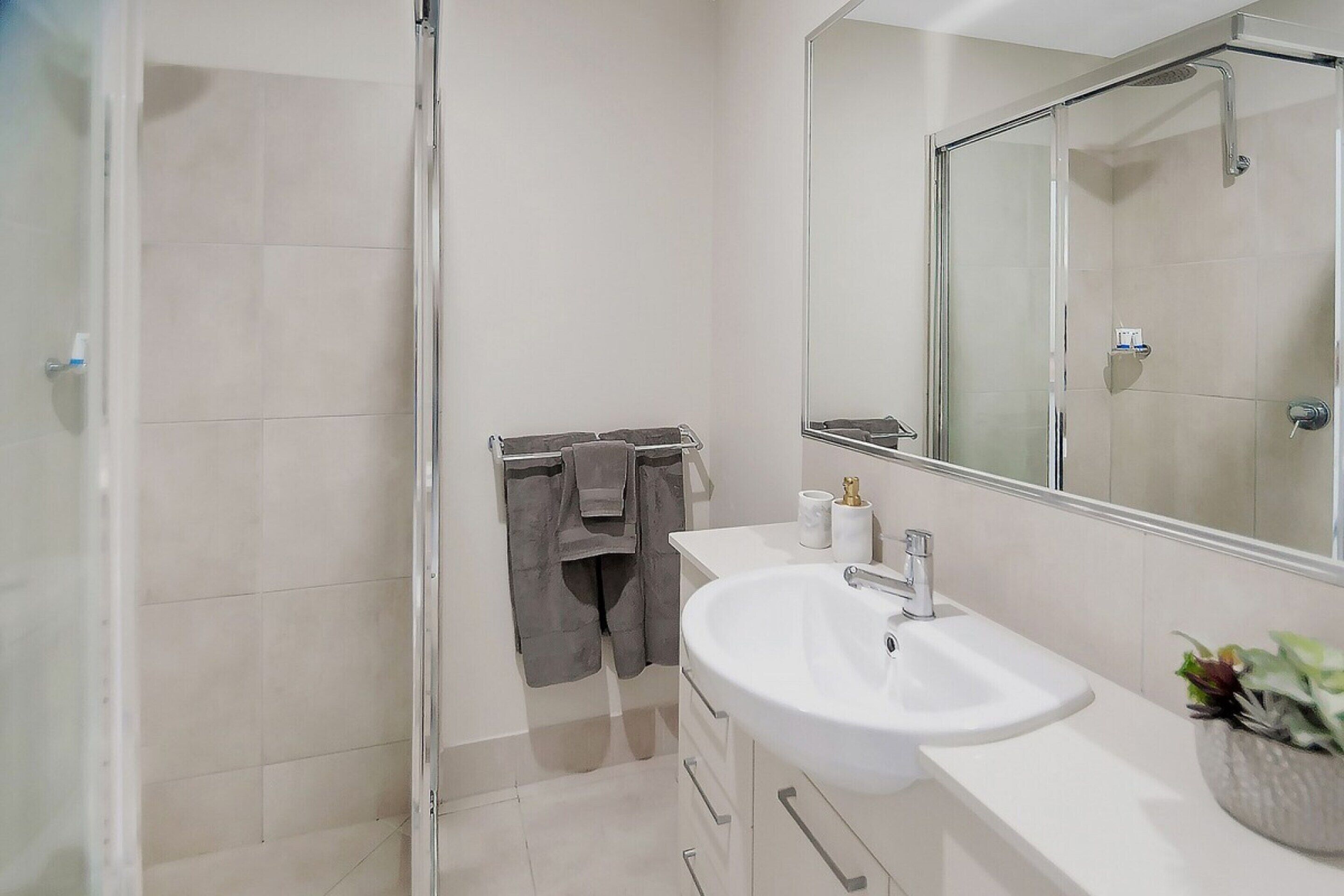 A modern bathroom with a glass shower enclosure, a white sink, and a large mirror.