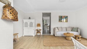 A living room with a white sofa, a round wooden coffee table, a wicker basket, and a woven rug. - Bright Coastal Townhouse With BBQ & Courtyard (Avoca Beach)