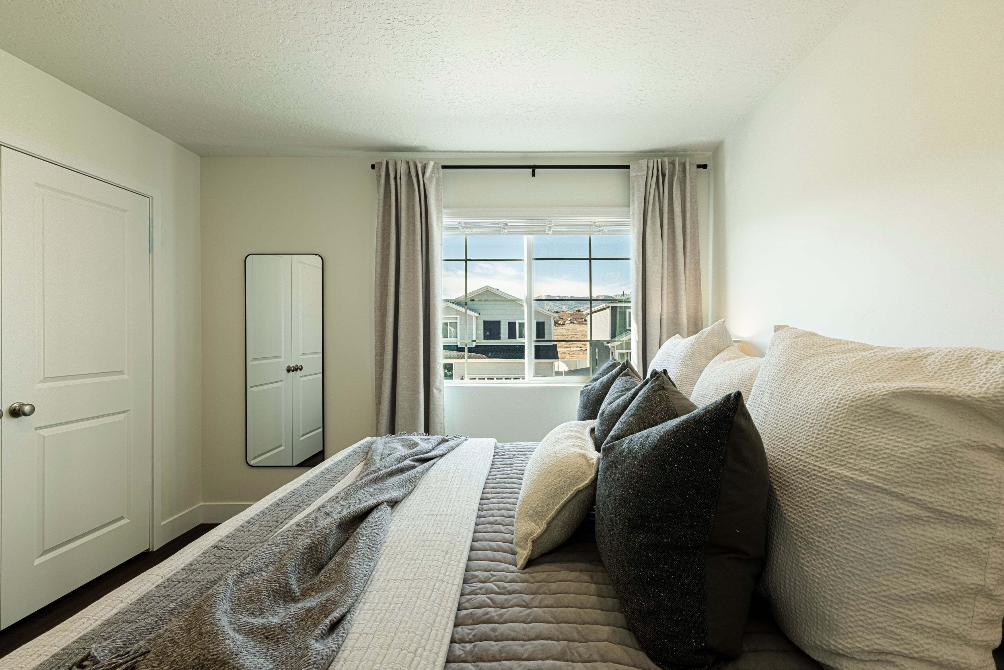 A bedroom with a bed, a window with curtains, a door, and a mirror.