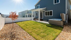 A modern two-story house with a covered patio, a hot tub, and a well-maintained lawn. - Park City Redbud Hideaway | Modern 6BR Mountain Retreat w/ Hot Tub & Views (Park City)