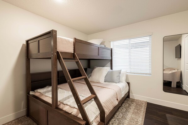 A bunk bed with a wooden ladder, a window with blinds, and a mirror on the wall.