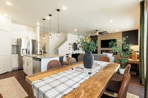 Une cuisine moderne équipée d’appareils électroménagers en acier inoxydable, un coin repas avec une table en bois et un espace de vie comprenant un canapé et un téléviseur.