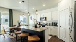 A modern kitchen with a large island, white cabinetry, stainless steel appliances, and pendant lighting. - Park City Redbud Hideaway | Modern 6BR Mountain Retreat w/ Hot Tub & Views (Park City)